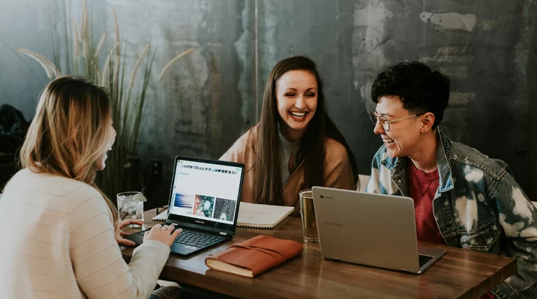 Três pessoas sentadas em volta de uma mesa com os seus laptop discutindo sobre os tipos de comunicação interna